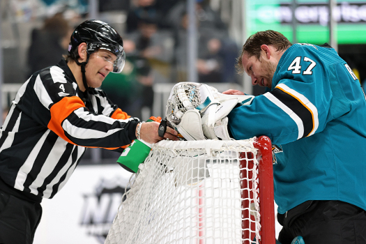 Referee Wes McCauley watches as Sharks goalie James Reimer inspects his catching glove