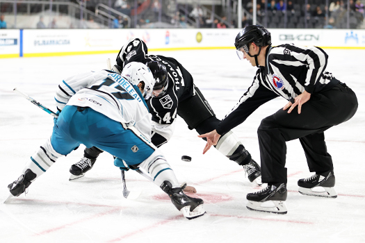 Linesman Alex Ledovskiy (21) drops the puck on a faceoff between Thomas Bordeleau (17) and Jacob Moverare (44)